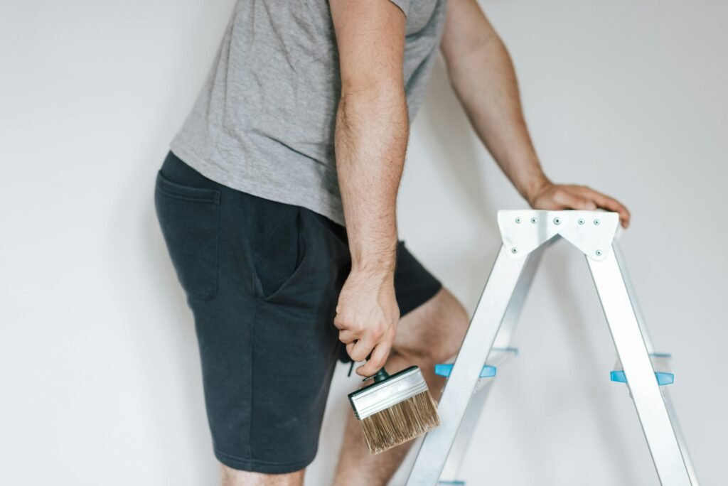 Side view of crop anonymous male decorator in casual clothes preparing to painting walls of light room while standing on stepladder